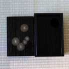 A pair of silver-toned sunburst earrings displayed on a black lacquered box next to its open black lid, set against a light beige woven straw mat background.