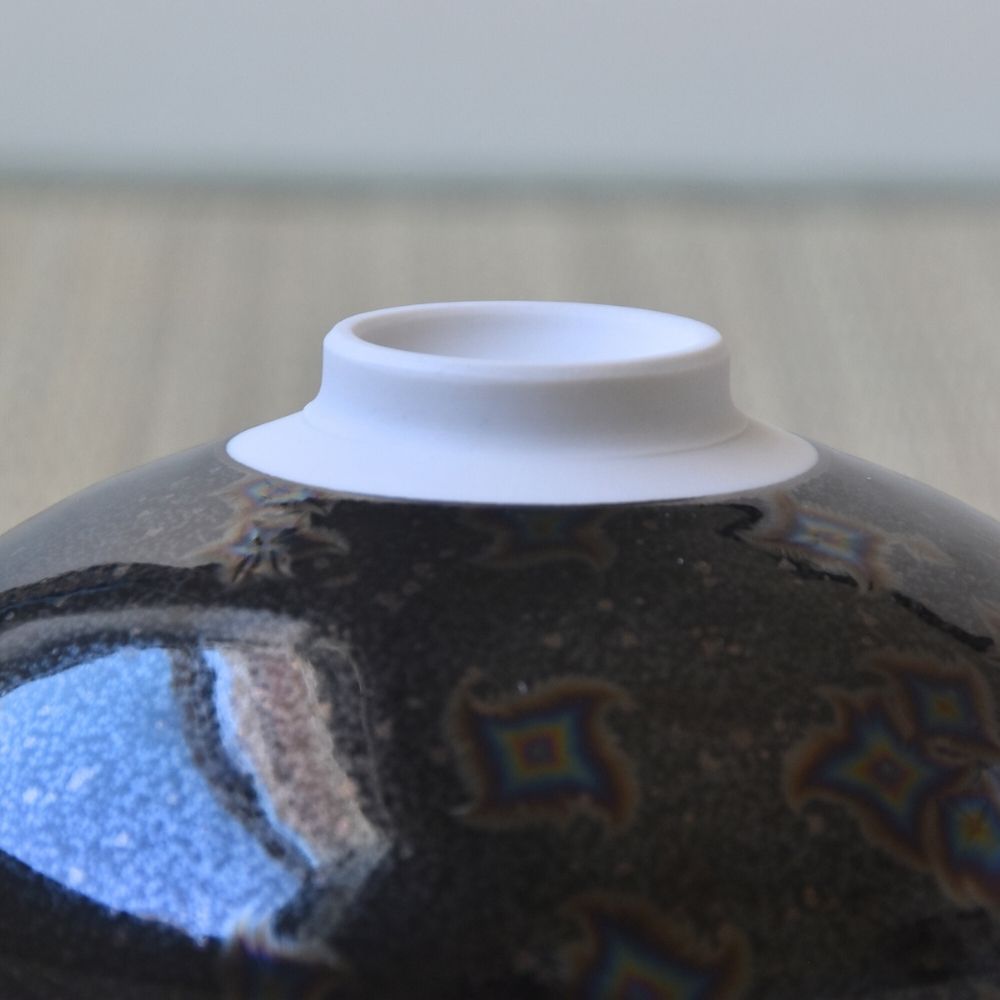 Close-up of a ceramic vase with decorative patterns and a white rim.