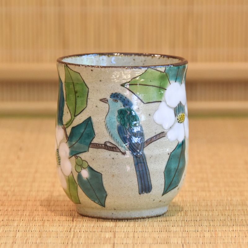 Ceramic cup with bird and floral design on a woven mat background