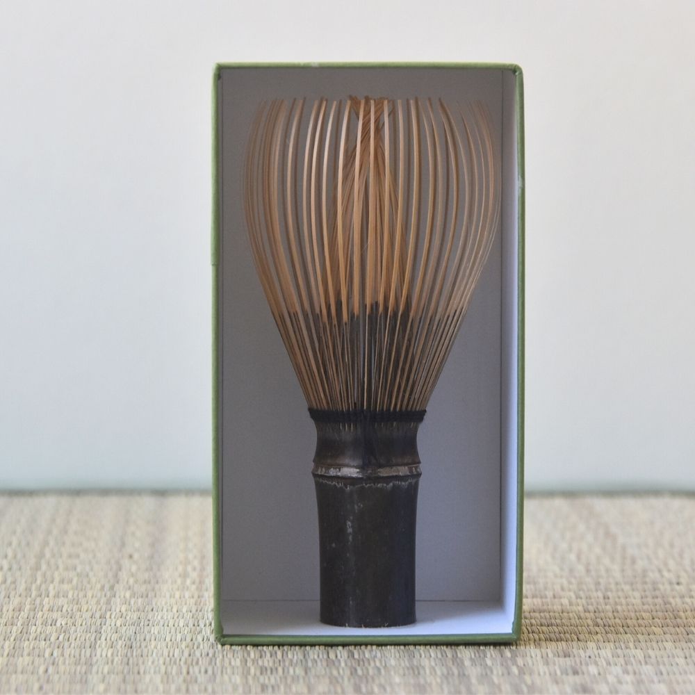 Traditional Japanese whisk (Chasen) in a box on a textured surface with a light background