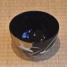 Black ceramic bowl with a design on a woven mat