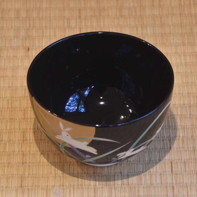 Black ceramic bowl with a design on a woven mat