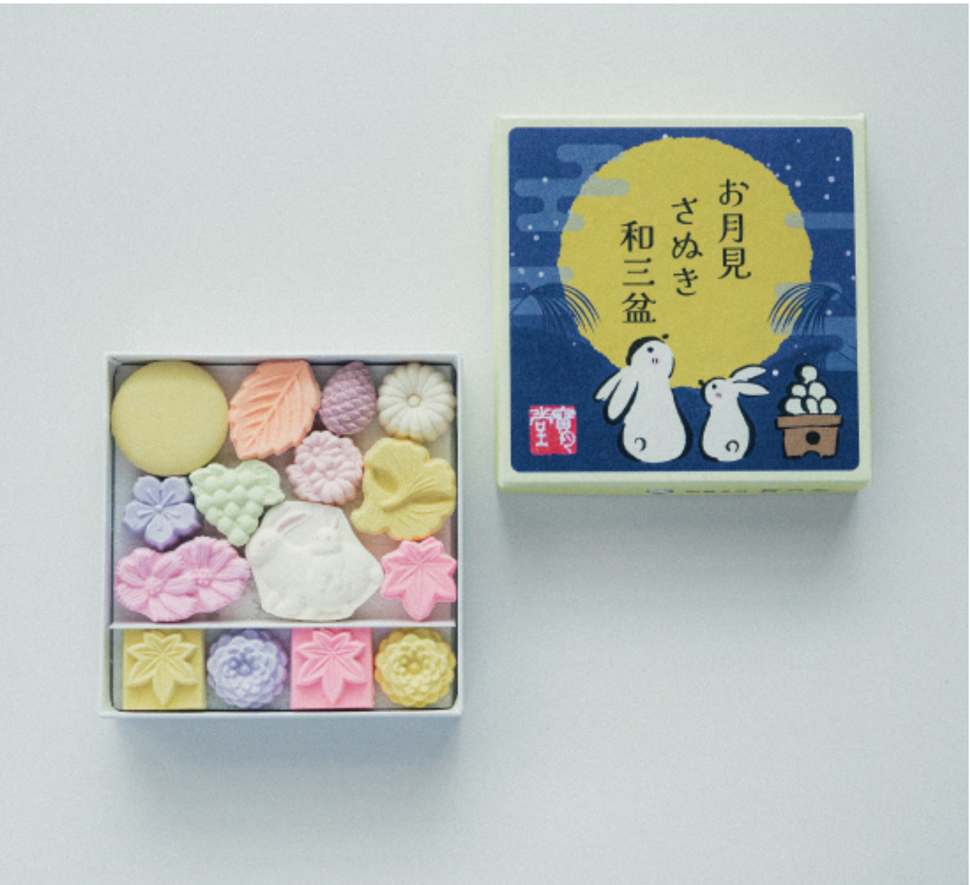 Box of colorful candy with a decorative box featuring cartoon characters and Japanese text on a light gray background.