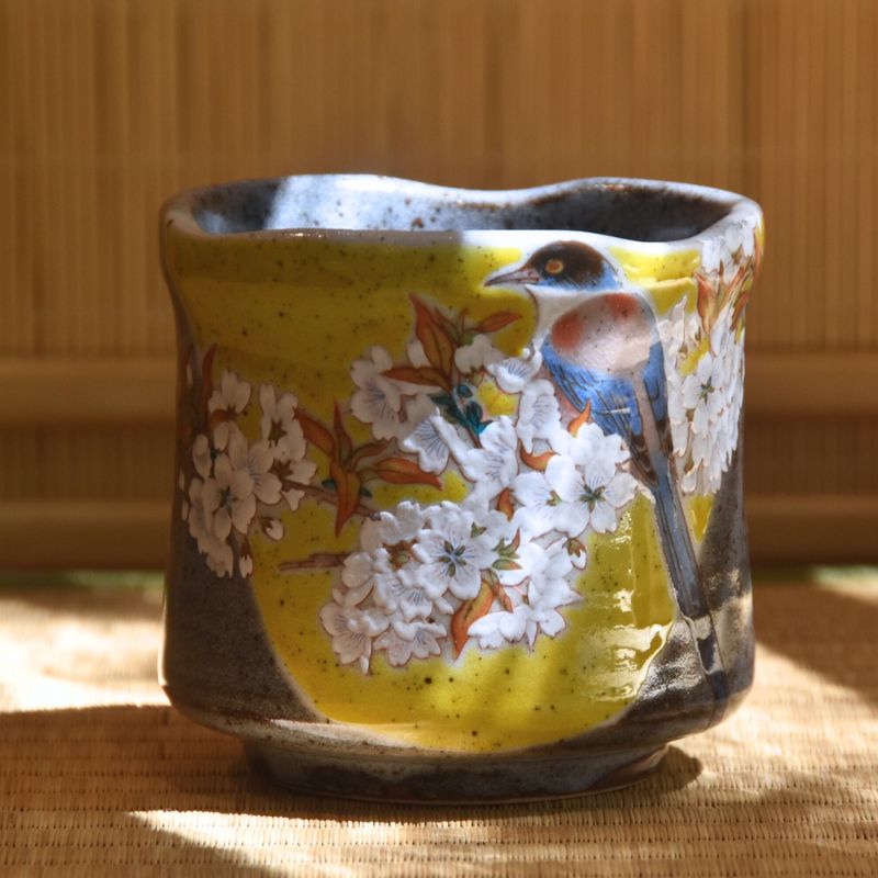 Ceramic cup with bird and floral design on a wooden surface