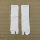 A pair of white tabi socks laid flat on a textured tan woven mat background.