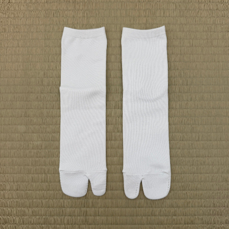 A pair of white tabi socks laid flat on a textured tan woven mat background.