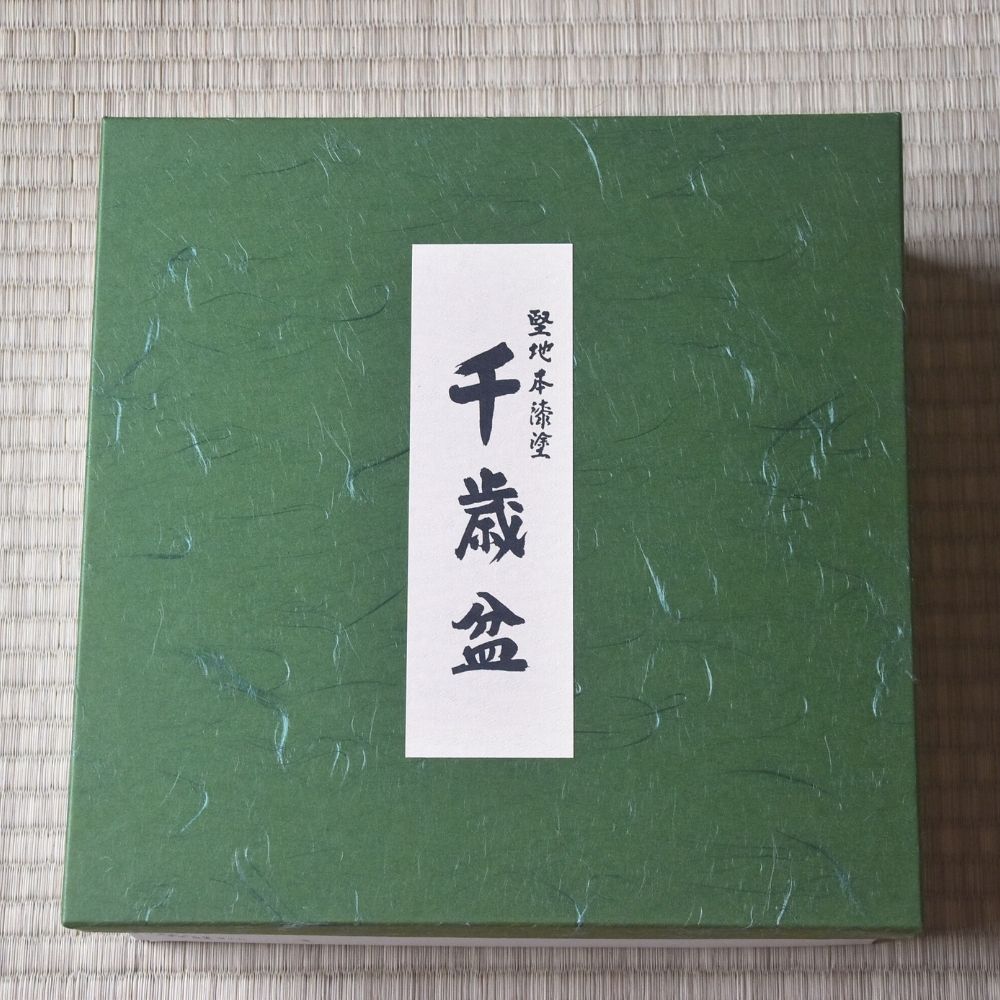 Green textured box with a white label featuring black text on a woven mat background