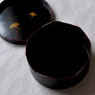 Black lacquerware containers with ginkgo leaf design on a textured surface