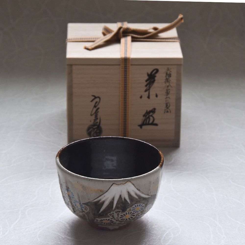 Ceramic cup with decorative patterns in front of a wooden gift box on a light background