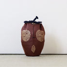 A brown fabric drawstring pouch with gold embroidered circular patterns and a dark navy cord closure, standing upright on a textured surface against a plain light background.