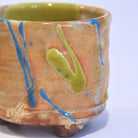 Ceramic pot with orange glaze and blue and green accents on a white background