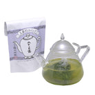 Glass teapot with green liquid and a package of tea bags on a white background