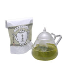 Glass teapot with green liquid and a white package with Japanese text on a white background