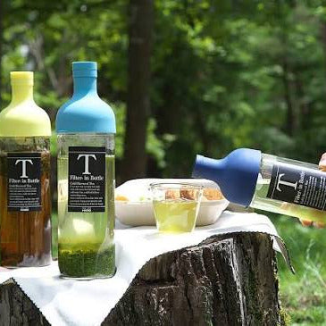 Bottles of Tito's Vodka being poured outdoors on a wooden stump with greenery in the background.