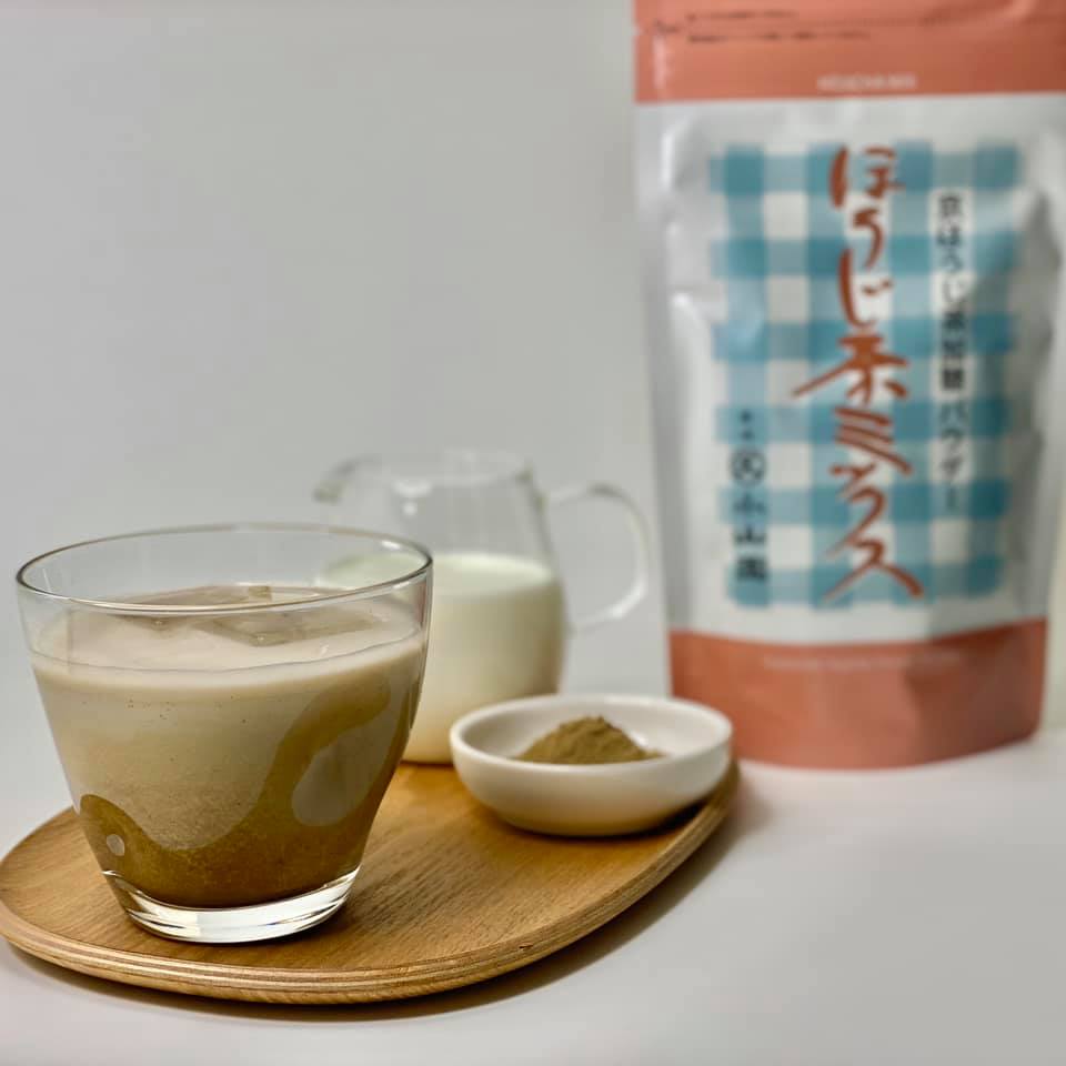 Glass of latte with a small bowl of cream and a package of coffee powder on a wooden tray.