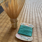 Bamboo whisk and spool of green thread on a woven mat