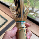 Bamboo whisk held by a hand with a blurred outdoor background