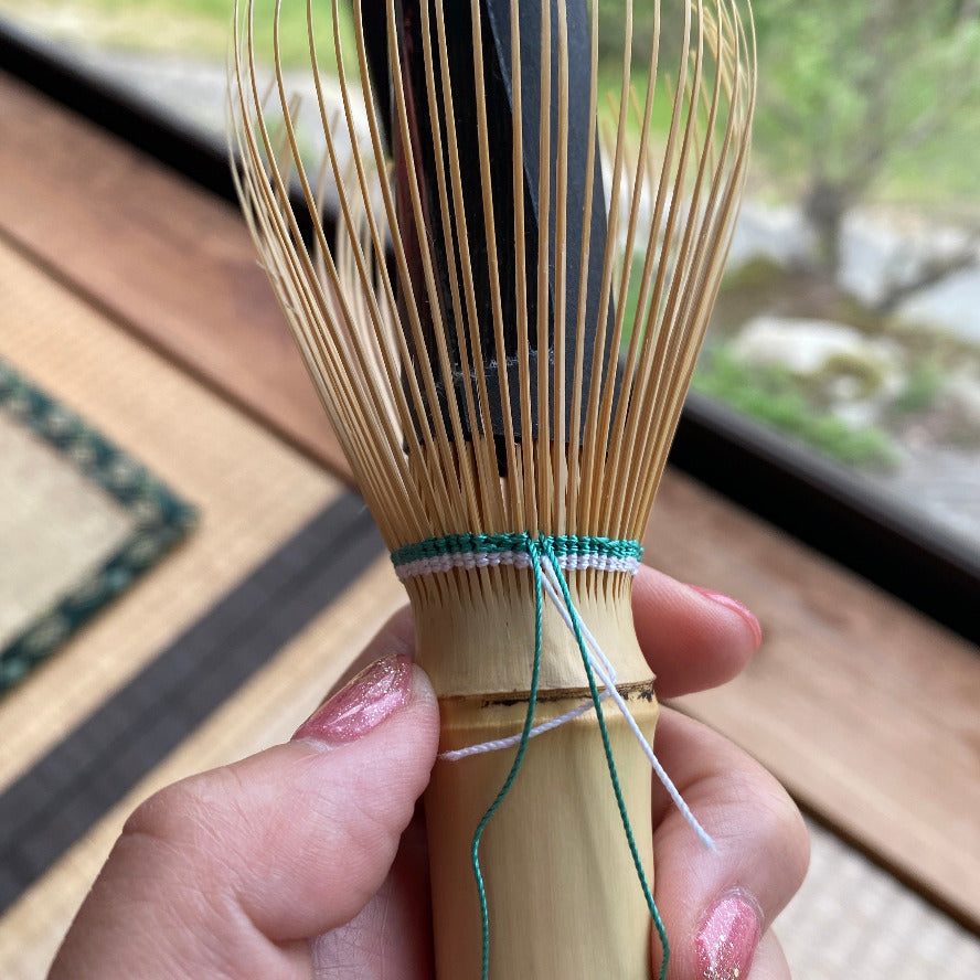 Bamboo whisk held by a hand with a blurred outdoor background