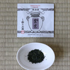 Tea leaves in a white bowl with a tea bag packaging on a woven mat
