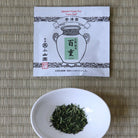 White bowl with green tea leaves and a tea package on a woven mat