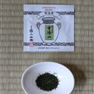 Tea packaging and a white bowl with tea leaves on a woven mat