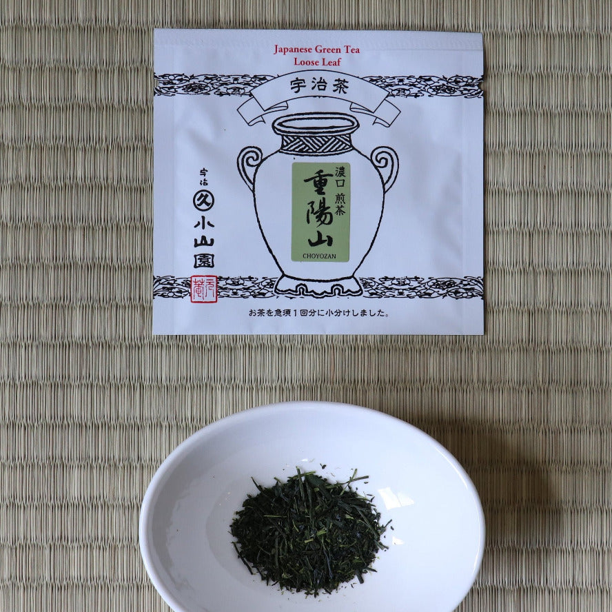 Tea packaging and a white bowl with tea leaves on a woven mat