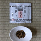 Tea leaves in a white bowl next to a tea package on a textured surface