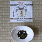 Tea leaves in a small white bowl next to a tea package on a woven mat