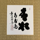 Calligraphy piece on a white sheet with black ink on a textured brown background