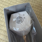 White product wrapped in plastic with a logo, inside an open box on a woven mat background