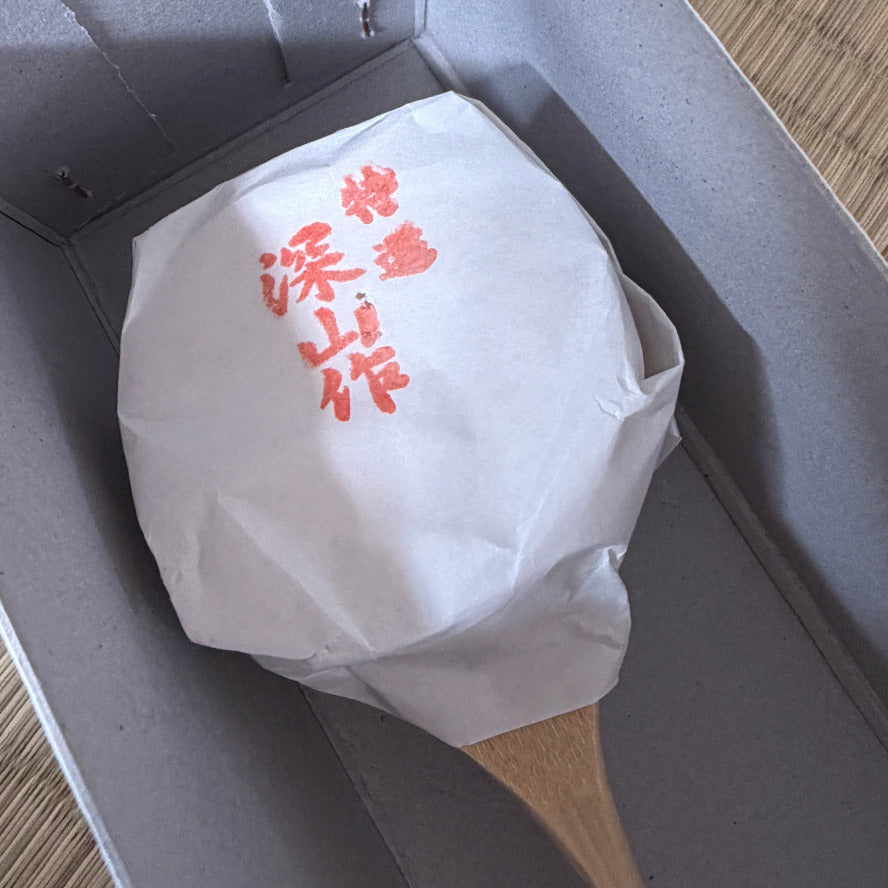 White paper-wrapped item with red text in a gray box on a wooden surface