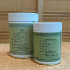 Two green tea containers with labels on a wooden surface