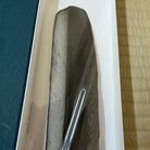 A dark gray textured stone or slate decorative piece inside a white rectangular tray, with a blue textured surface on the left and a tan woven mat on the right.