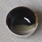 Ceramic bowl with dark interior and light exterior on a textured surface