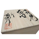 Wooden block with Japanese calligraphy and a red stamp on a white background