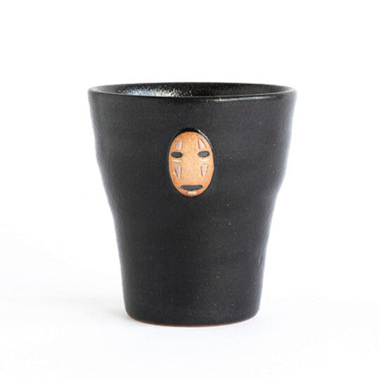 Black cup with a face design on a white background, featuring Studio Ghibli branding.