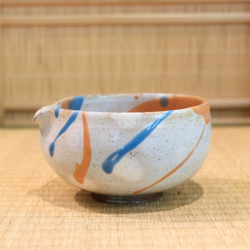 Ceramic bowl with blue and orange stripes on a woven mat