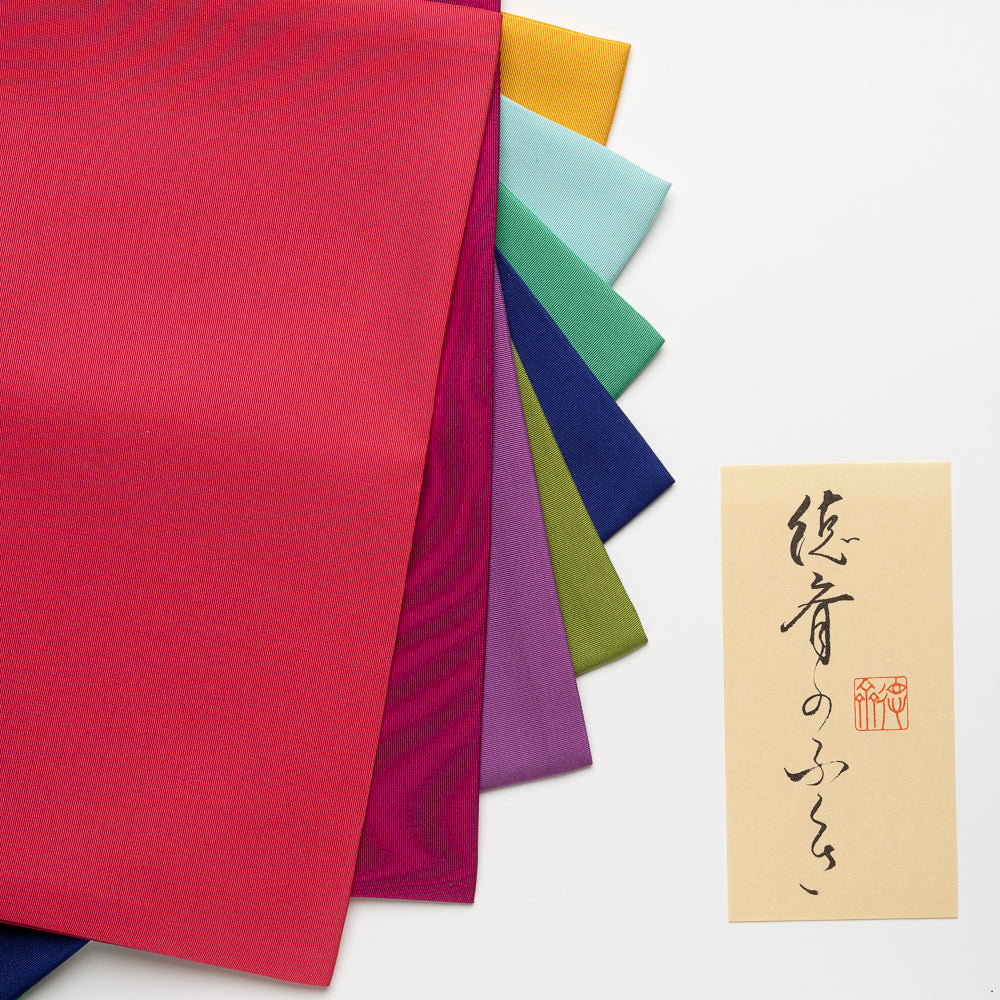 Colorful paper sheets in various colors with a small card featuring Japanese text on a white background.
