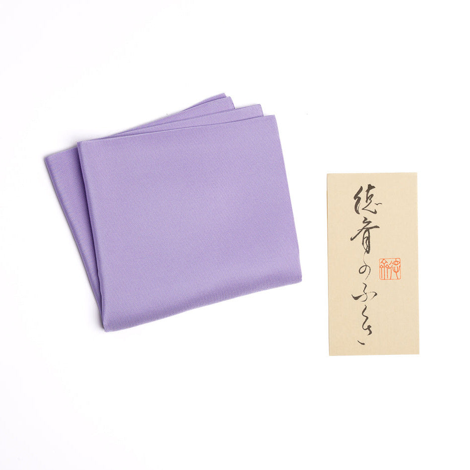 Folded purple fabric with a small beige card featuring Japanese text and a red stamp on a white background