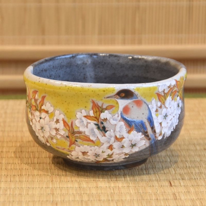 A Kutani Ware matcha bowl with a vibrant yellow exterior, featuring a detailed hand-painted design of a bird among cherry blossoms.