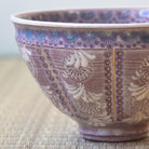 Ceramic bowl with intricate purple and white floral patterns on a textured surface.