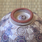 Close-up of a ceramic jar with floral patterns and a red lid on a woven mat background.