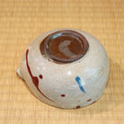 Ceramic bowl with speckled glaze and brown accents on a woven mat