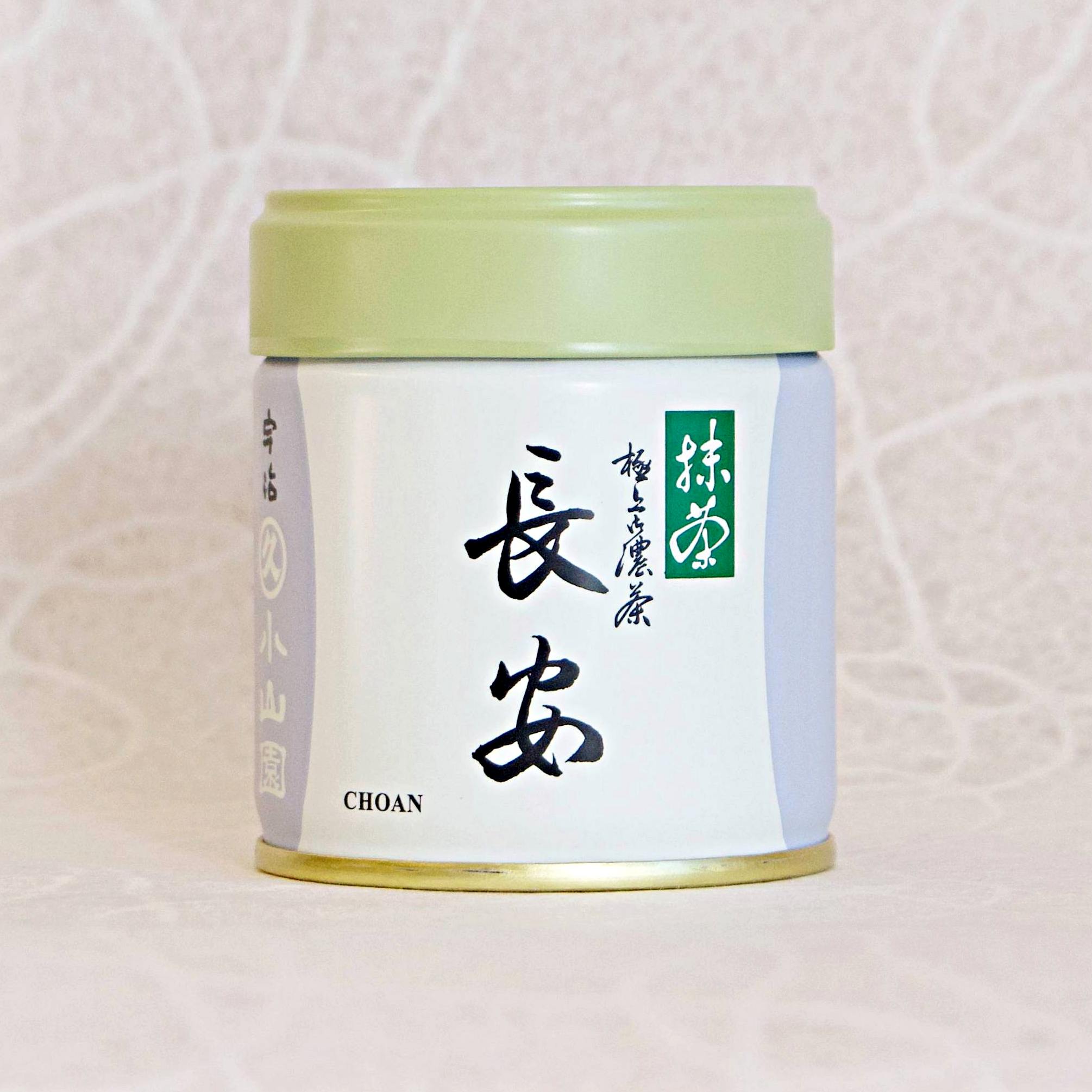 A canister of CHOAN Ceremonial Grade Matcha with Japanese characters printed on the label, placed against a patterned background.