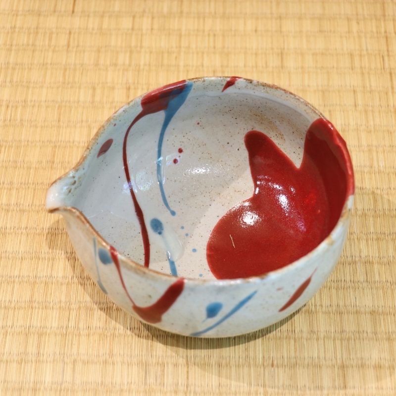 Ceramic bowl with red and blue abstract design on a woven mat