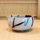 Ceramic bowl with blue and black designs on a woven mat