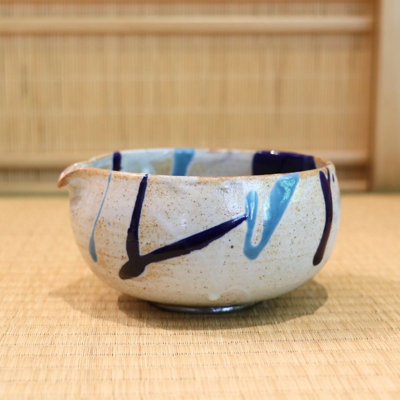 Ceramic bowl with blue and black designs on a woven mat