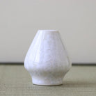 White textured vase on a light green surface with a neutral background