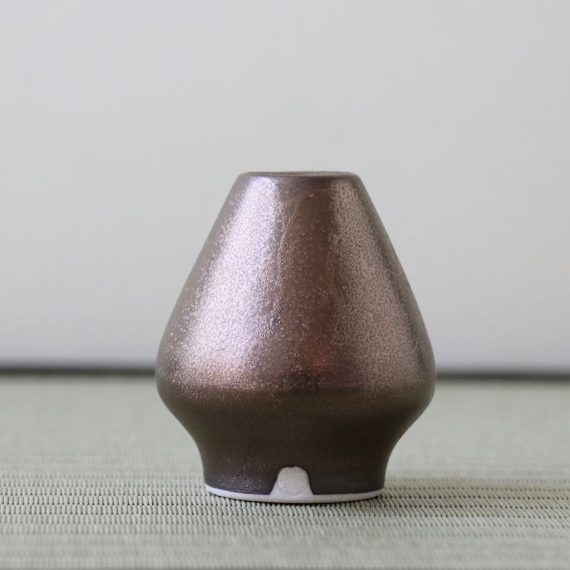 Brown ceramic vase on a textured surface with a neutral background