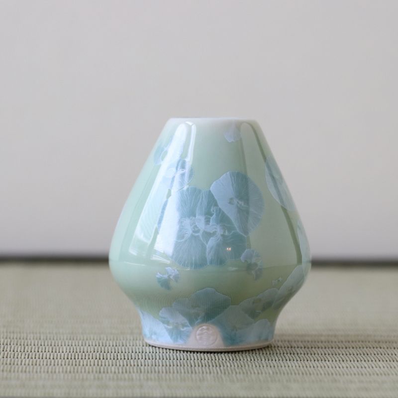 Green ceramic whisk stand with floral patterns on a neutral background